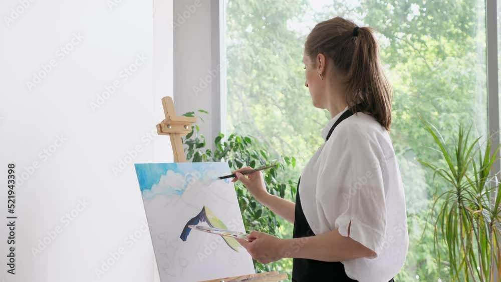 Mature woman paints sky watercolor on canvas with paintbrush. Skilled female artist enjoys painting on wooden easel in comfortable atmosphere closeup Mature woman paints sky watercolor on canvas with paintbrush. Skilled female artist enjoys painting on wooden easel in comfortable atmosphere closeup