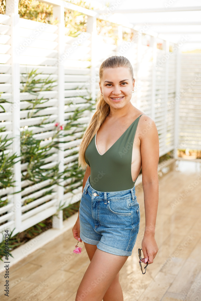 Blond woman beautiful face tanned skin dressed in green top and denim shorts fashion clothing style summer clothes collection, summer and leisure
