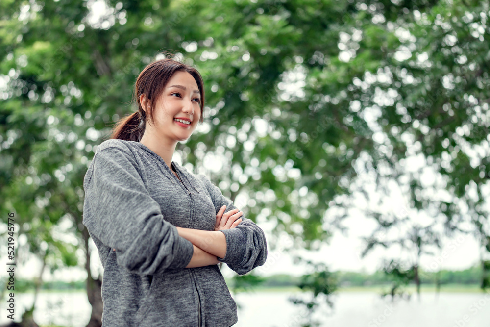 Happy young asian woman smiling before workout sport exercises outdoors on a background of park trees. Healthy lifestyle well being wellness happiness concept