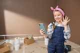 A little girl talks through a video camera on her phone with a friend. Child waves to smartphone shows new apartment during renovation enjoys painting walls.