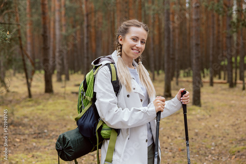 Young beautiful blonde woman trains tekking in woods with poles. Woman enjoys outdoor sports is smiling contentedly. photo