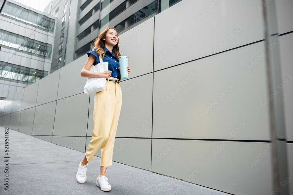 Asian beautiful business woman confident smiling with cloth bag holding steel thermos tumbler mug water glass she walking outdoors on street near modern building office, Happy female look forward
