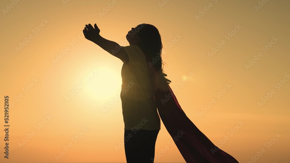 girl superhero with long hair red cape wind sunset. brave superhero ready help. superhero background sky rays sun. childhood dream teenager. child stretches hands sun. happy childhood superhero game