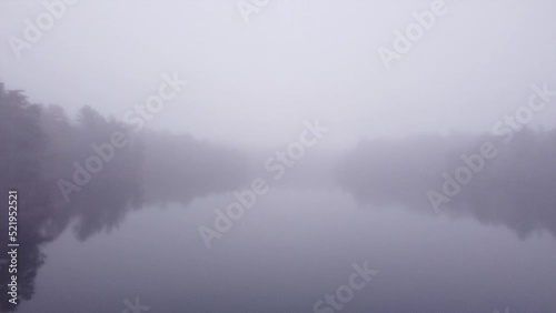 Flying over a pond during heavy fog, with haunting silhouettes of trees lining the shores. photo