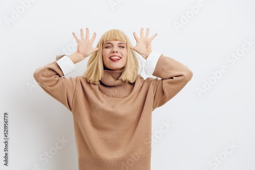  Horizontal photo, a woman on a white background in a beige sweater with beautiful blond hair and a smile raising her hands up has fun