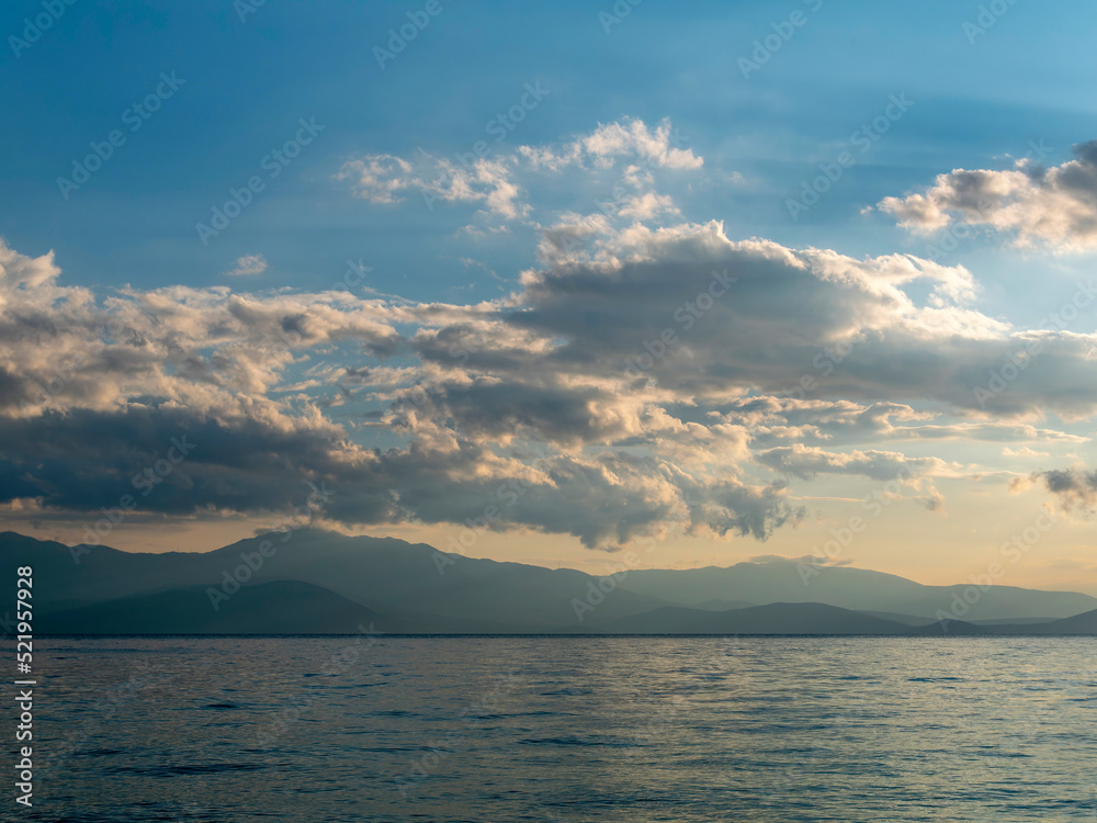 Cloudy sky above the sea and mountains in the background of the horizon. The change of weather is continuous in all seasons.