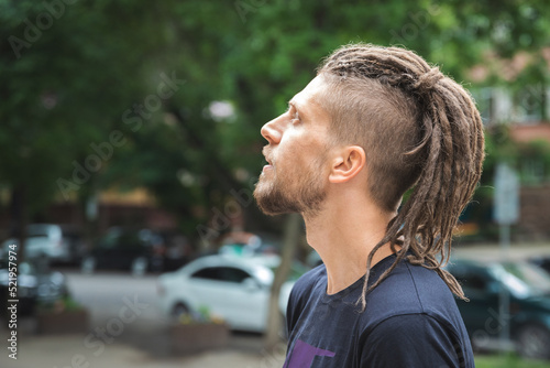 Side view of a caucasian man with dreadlocks and sidecut on a summer street. photo