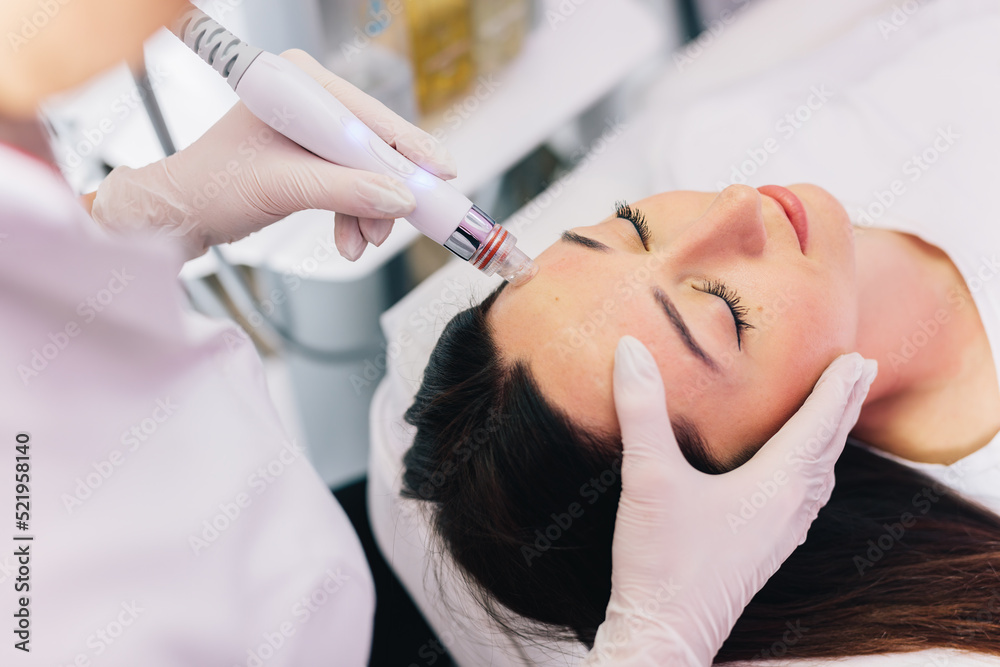 Cosmetologist doing hydrafacial treatment on woman face - obrazy, fototapety, plakaty 