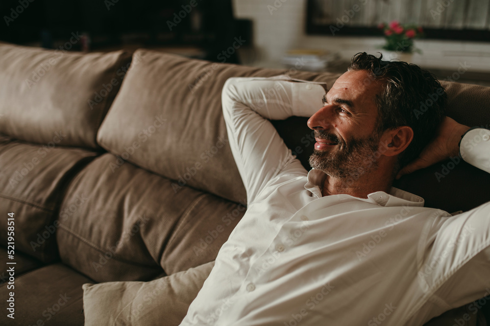 Smiling businessman day dreaming on sofa at home