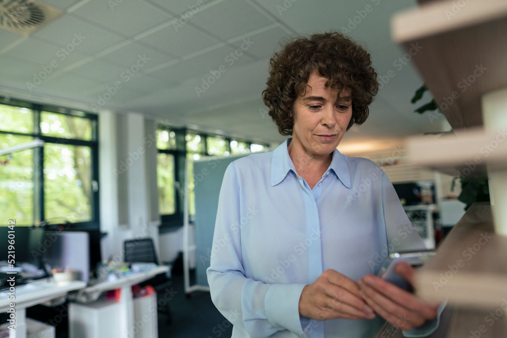 Businesswoman text messaging through smart phone in office Businesswoman text messaging through smart phone in office