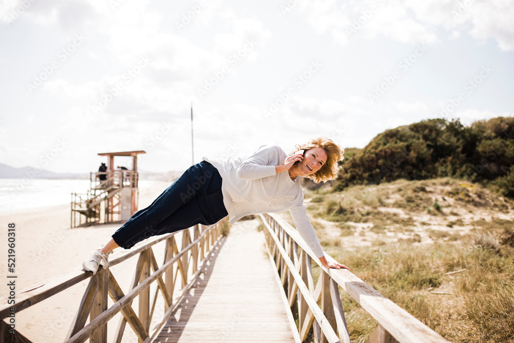 Mature woman leaning railings and talking through smart phone at beach Mature woman leaning railings and talking through smart phone at beach