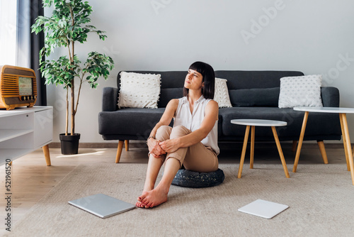 Thoughtful woman sitting on hassock at home