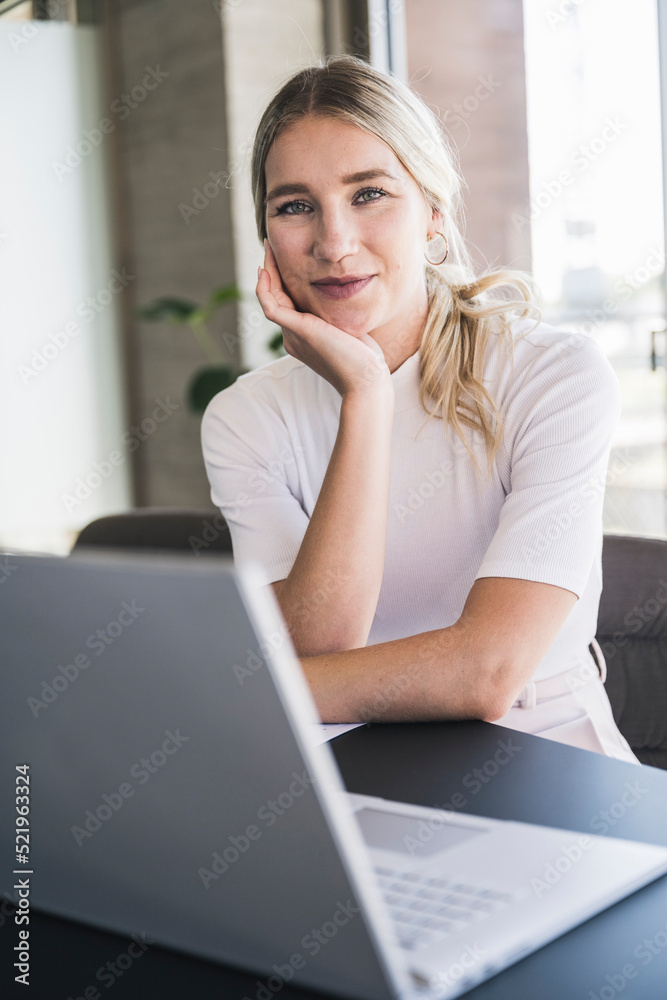 Blond businesswoman leaning on elbow sitting at desk in office Blond businesswoman leaning on elbow sitting at desk in office