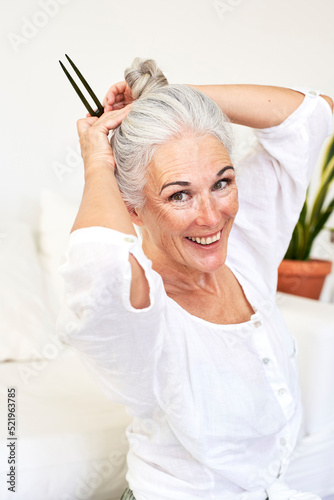 Happy woman with hair clip tying bun sitting in living room