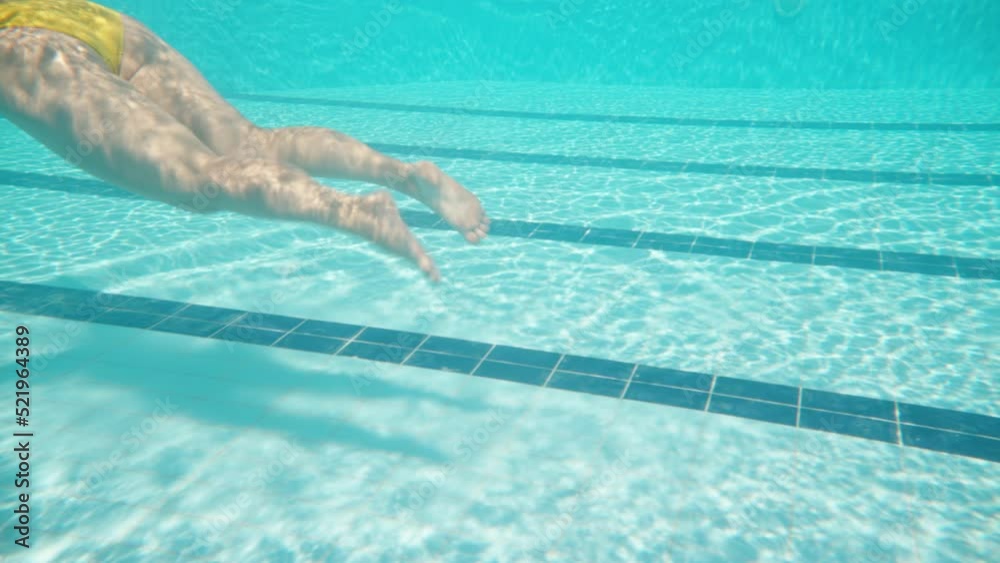 Swimming pool and camera underwater. A girl in a yellow swimsuit, swimming, the camera follows her and goes under the water.