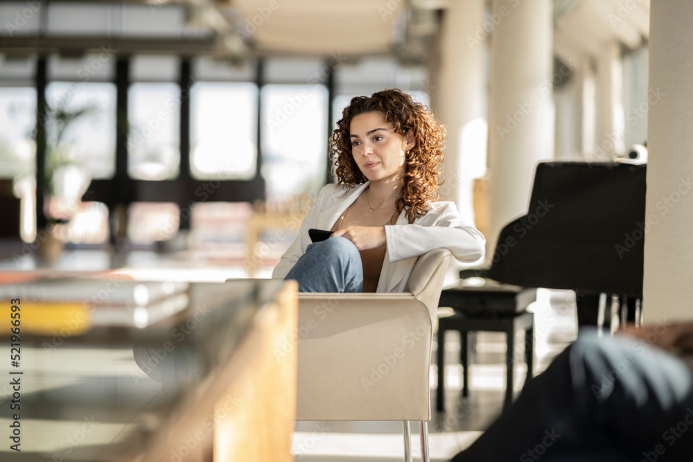 Thoughtful businesswoman with curly hair sitting on chair in office Thoughtful businesswoman with curly hair sitting on chair in office
