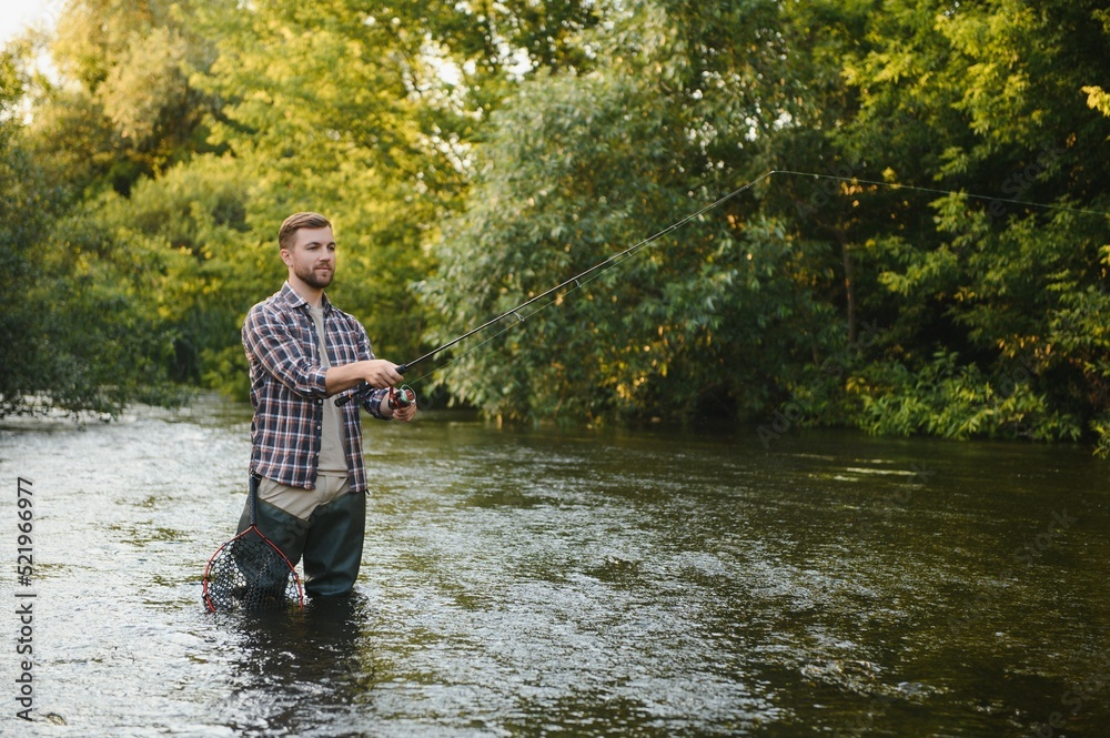 Man with fishing rod, fisherman men in river water outdoor. Catching trout fish in net. Summer fishing hobby