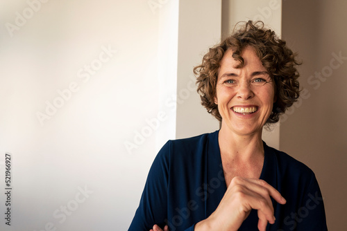 Cheerful real estate agent with curly hair in front of wall photo