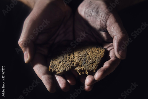 Hungry man holding bread on a black background, hands with food close-up. Dirty hands of a starving poor man on a dark background