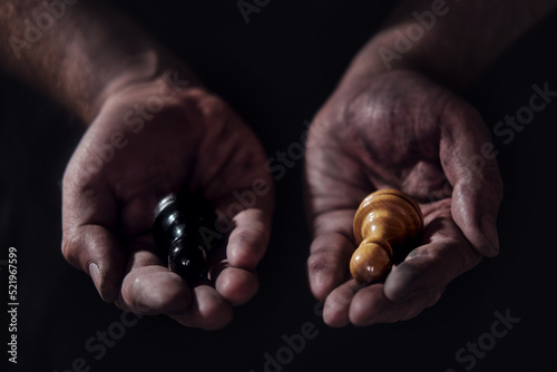 Hands holding black and white chess pieces on a dark background. Pawns in the hands of a man on a black background.