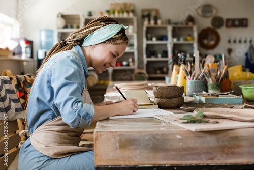 Smiling craftsperson drawing on sketch pad at art studio photo