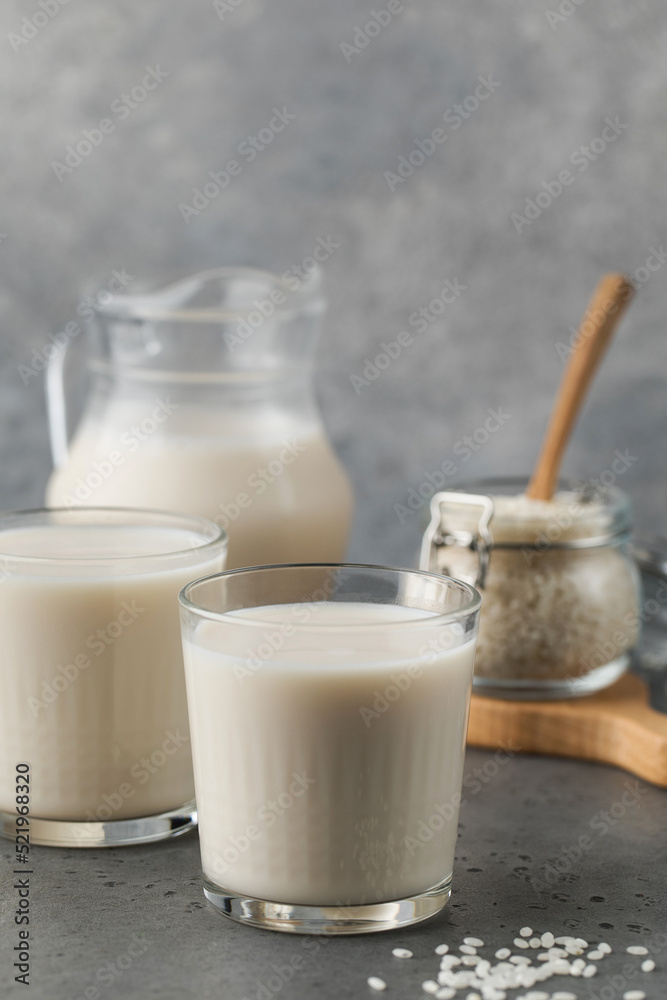 Glasses of vegetable rice milk and a jug on a gray background. Vegetarian food, lactose free milk. Glasses of vegetable rice milk and a jug on a gray background. Vegetarian food, lactose free milk.