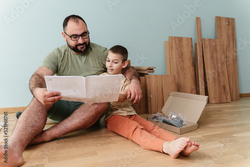 Happy father with son reading instruction manual sitting on floor at home