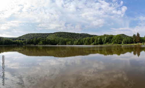 Panorama of a lake in the morning with a forest and a blue cloudy sky