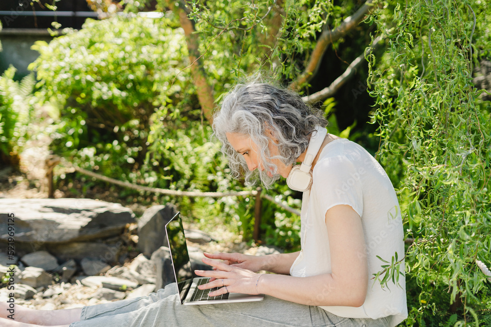 Freelancer using laptop by plants in park Freelancer using laptop by plants in park