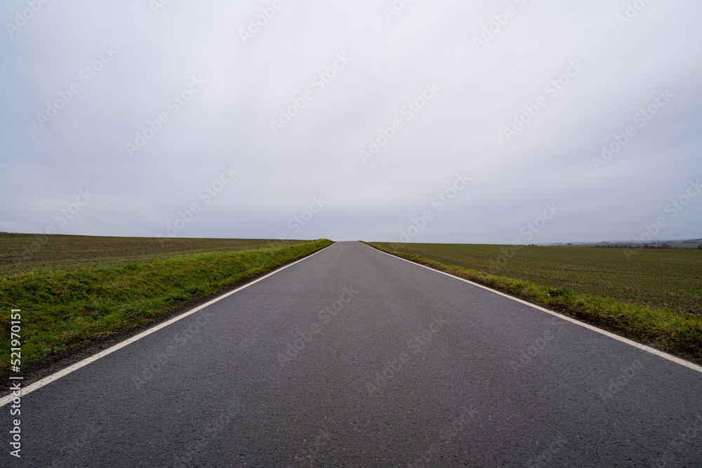 Asphalt country road between agricultural fields with a cloudy sky in autumn