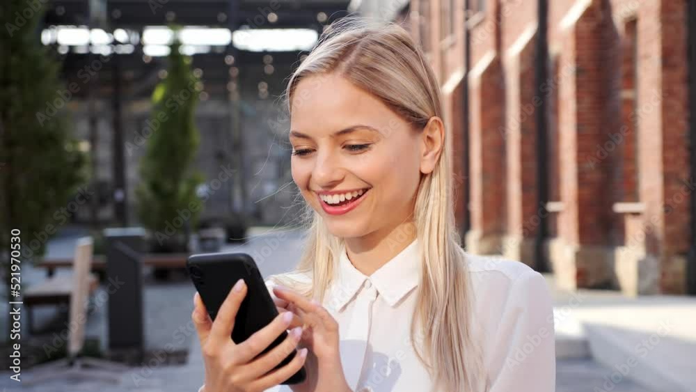Positive young woman in white shirt uses mobile phone chatting with friend in social media. Joyful lady blond browsing internet date app, enjoys texting on smartphone outdoor. New modern technologies. Positive young woman in white shirt uses mobile phone chatting with friend in social media. Joyful lady blond browsing internet date app, enjoys texting on smartphone outdoor. New modern technologies.