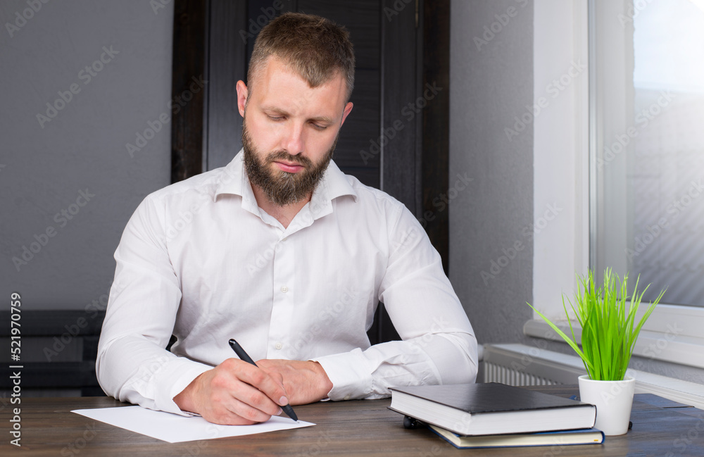 Young businessman is sitting at the table. A man in a shirt. Office worker. A man with a beard.