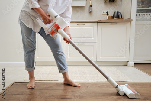 Woman with a wireless portable vacuum cleaner in the kitchen. Cleans the floor in an apartment with a vacuum cleaner with a battery