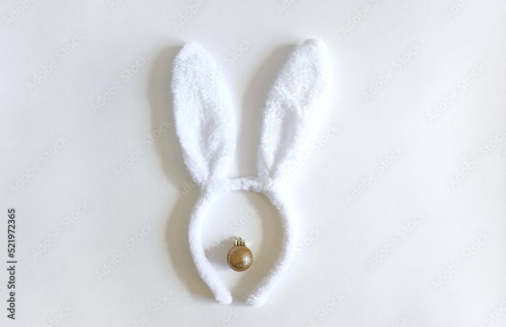 Obraz premium white rabbit ears and a golden Christmas ball on a white background, a symbol of the New Year of the rabbit 2023, the concept of Merry Christmas and holiday, Christmas rabbit ears copy, space