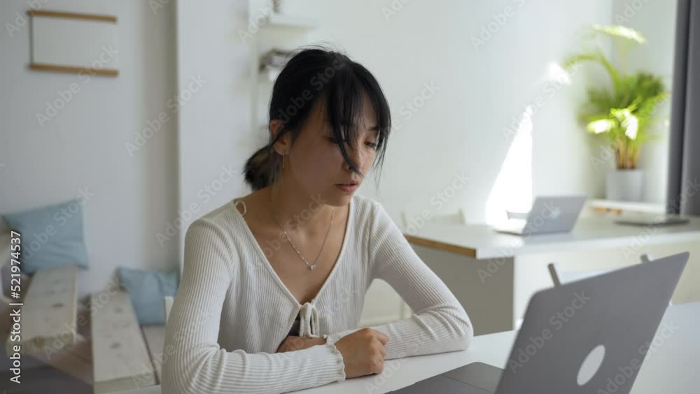 Young Asian employee talks to manager on video call via laptop sitting at desk in office. Woman waves head to agree looking at screen closeup Young Asian employee talks to manager on video call via laptop sitting at desk in office. Woman waves head to agree looking at screen closeup