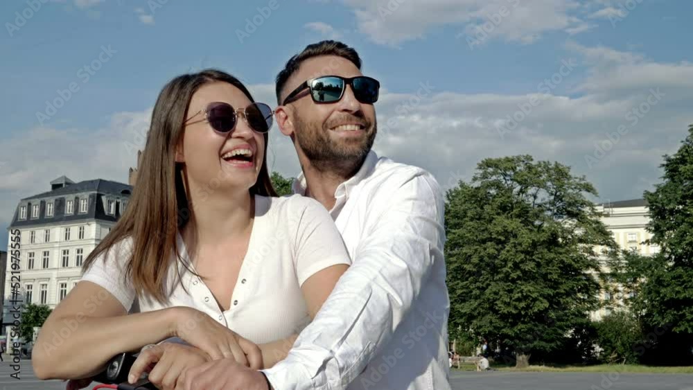 Summer portrait of a couple in love on an electric scooter. A man and a woman stand in the city square and look into the distance smiling happily. Summer portrait of a couple in love on an electric scooter. A man and a woman stand in the city square and look into the distance smiling happily.