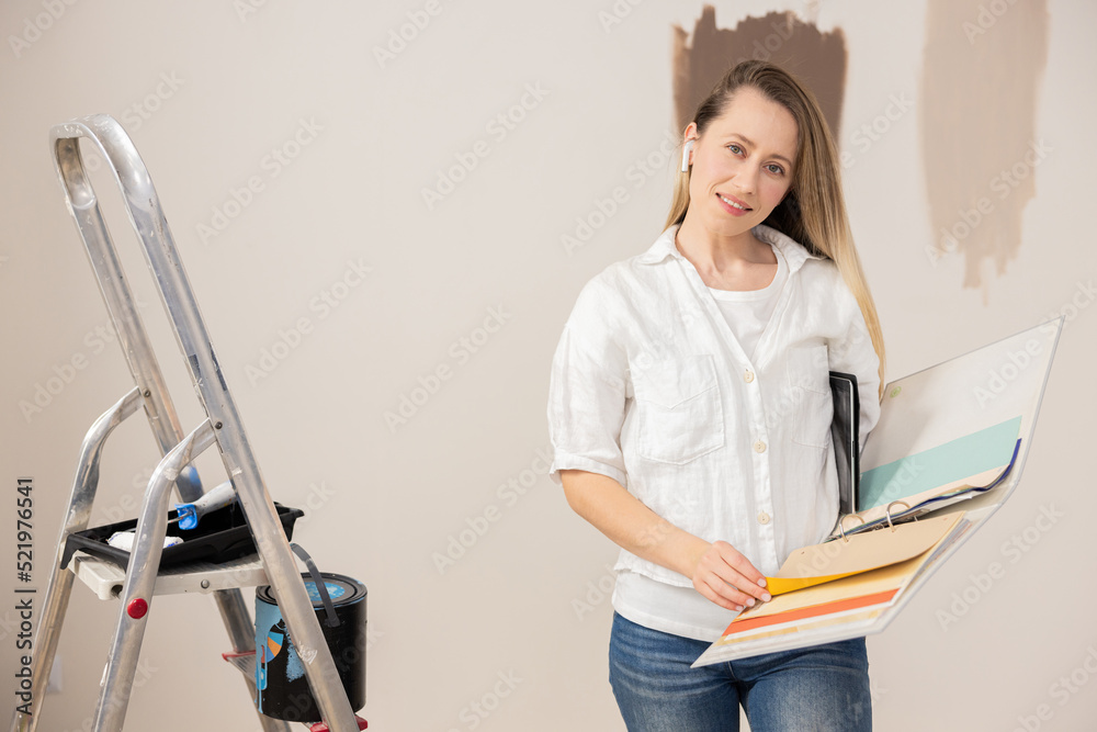 Beautiful female designer dressed in white t-shirt and shirt, holds a folder with colored sheets in hands - a paint palette. The girl has an earpiece in her ear, as she must always be on the phone. Beautiful female designer dressed in white t-shirt and shirt, holds a folder with colored sheets in hands - a paint palette. The girl has an earpiece in her ear, as she must always be on the phone.