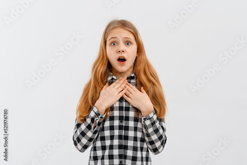 I can not believe it. Excited surprised teen girl looks with terror at camera as notices something unexpected or hears bad news, standing in casual shirt over white background