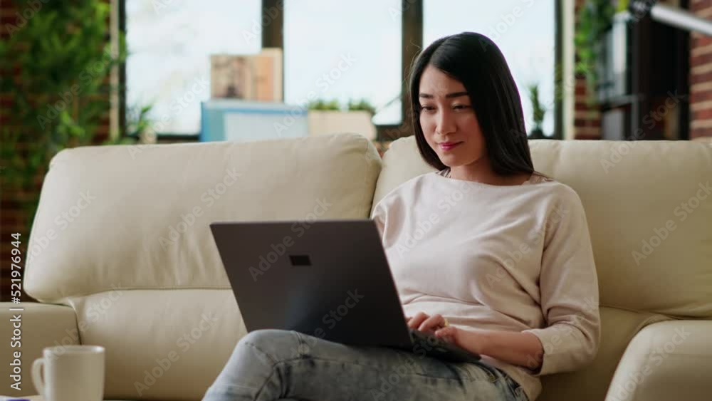 Smiling office worker at home working remotely on laptop while sitting on sofa in living room. Young adult person doing remote work on modern portable computer while at home. Smiling office worker at home working remotely on laptop while sitting on sofa in living room. Young adult person doing remote work on modern portable computer while at home.