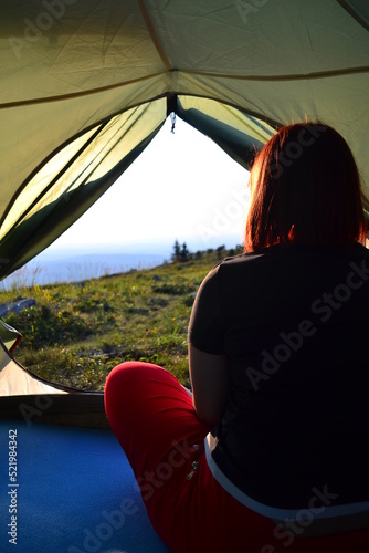 a girl sits in a tent and looks at a beautiful landscape