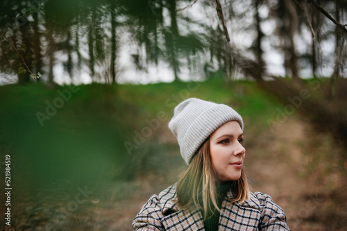 Portrait of young woman in coat and knitted cap in autumn nature, walking in forest. © Halfpoint