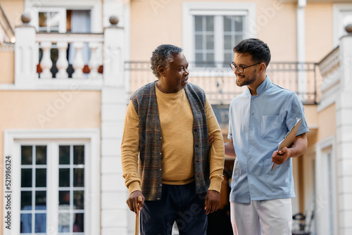 Male nurse talks to senior black man outdoors at residential care home.