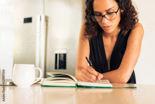 Focused freelancer writing notes in diary on kitchen island