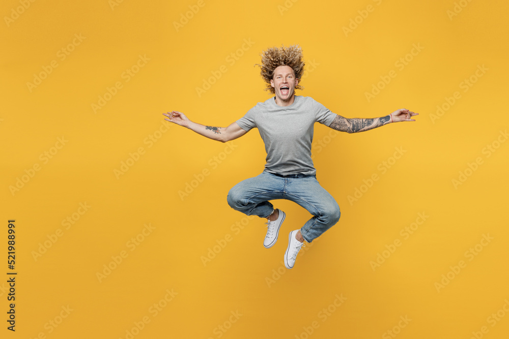 Full body young spiritual cheerful fun man 20s he wearing grey t-shirt holding spread hands in yoga om aum gesture relax meditate try to calm down jump high isolated on plain yellow backround studio