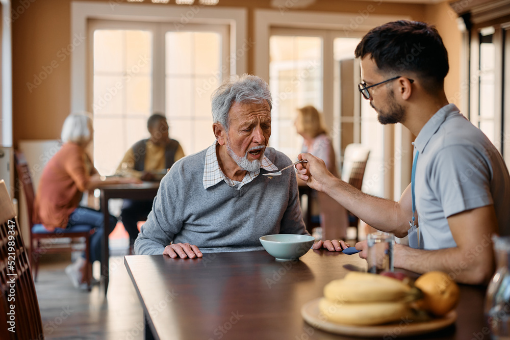 Old man eats with help of caregiver during lunch time at nursing home.