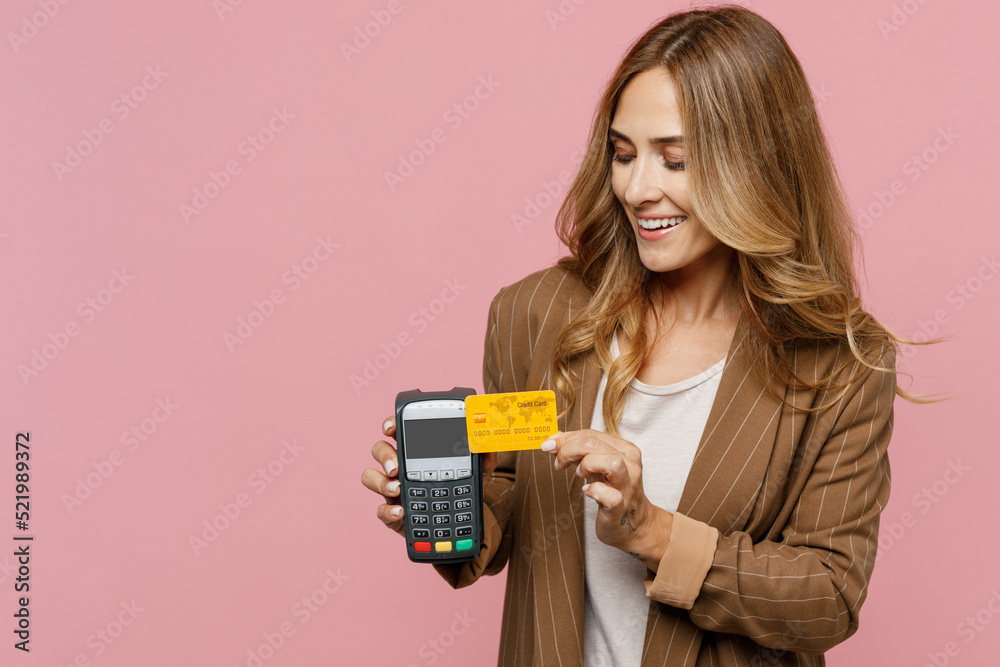 Young fun successful employee business woman 30s she wear casual brown classic jacket hold wireless bank payment terminal to process acquire credit card isolated on plain pastel light pink background. Young fun successful employee business woman 30s she wear casual brown classic jacket hold wireless bank payment terminal to process acquire credit card isolated on plain pastel light pink background.