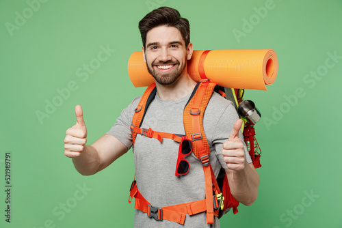 Young fun traveler white man carry backpack stuff mat show thumb up isolated on plain green background. Tourist leads active healthy lifestyle walk on spare time. Hiking trek rest travel trip concept. #521989791