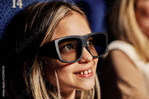 Close-up portrait of preteen Caucasian girl wearing polarized 3D eyeglasses enjoying watching movie at cinema