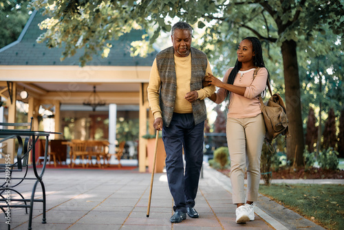 Obraz na plátne Happy African American woman walks with her senior father while visiting him at nursing home