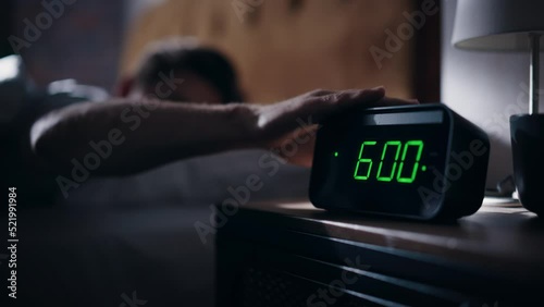 Man Wakes Up, Turns off Alarm Clock with Frustration. Early Rising Productive Man Ready Start a Day full of New Problems. Focus on the Clock Showing Six A.M. Bedside Nightstand bedroom Apartment photo
